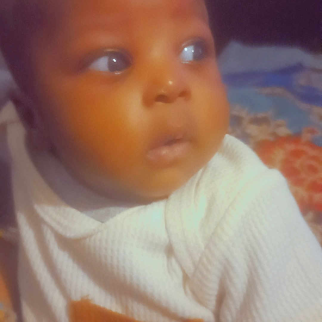 Siradji a rejoint le concours — aidez-le/la à gagner de superbes lots ! baby, child, closeup, cute, expression, eyes, face, head, human, indoor, infant, knitwear, looking_away, orange_pocket, person, portrait, soft_lighting, warm_colors, white_clothing, young_child