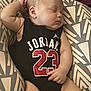 baby, sleeping, infant, black_clothing, jordan, number_23, cushion, patterned_cushion, arm_up, chubby_arm, peaceful, indoors, child, soft_light, relaxed, cute, portrait, resting, one_person, closeup
