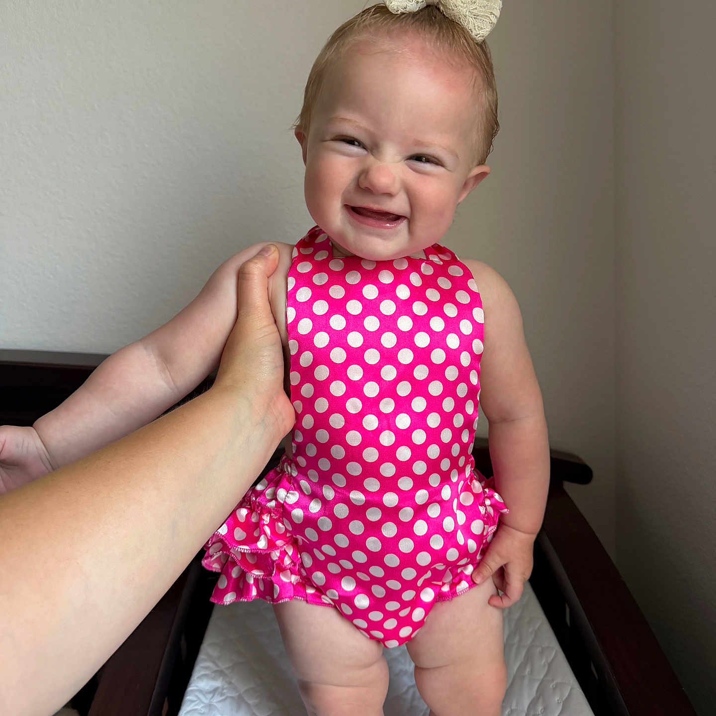 Adalynn is registered to the contest to win money with this photo: baby, child, infant, smile, grin, pink_swimsuit, polka_dot, bow, hair_tie, hand, changing_table, indoor, light_skin, cute, standing, person, one_child, happy, clothing, human