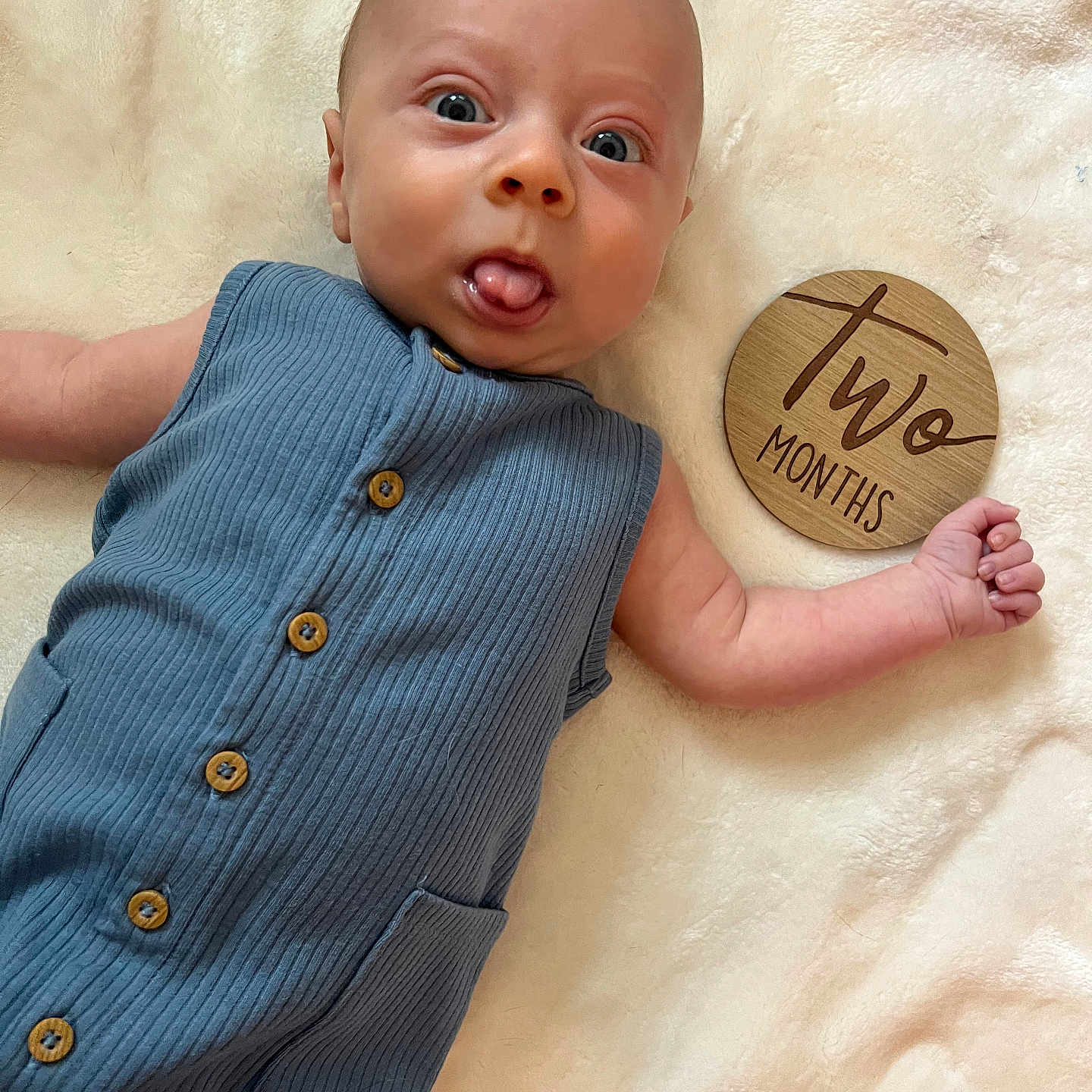Koen joined the competition — help win amazing prizes! baby, blanket, blue_clothing, buttoned_clothing, child, cute, expression, face, hand, indoor, infant, lying_down, newborn, portrait, romper, skin, soft_texture, tongue_out, two_months, wooden_sign