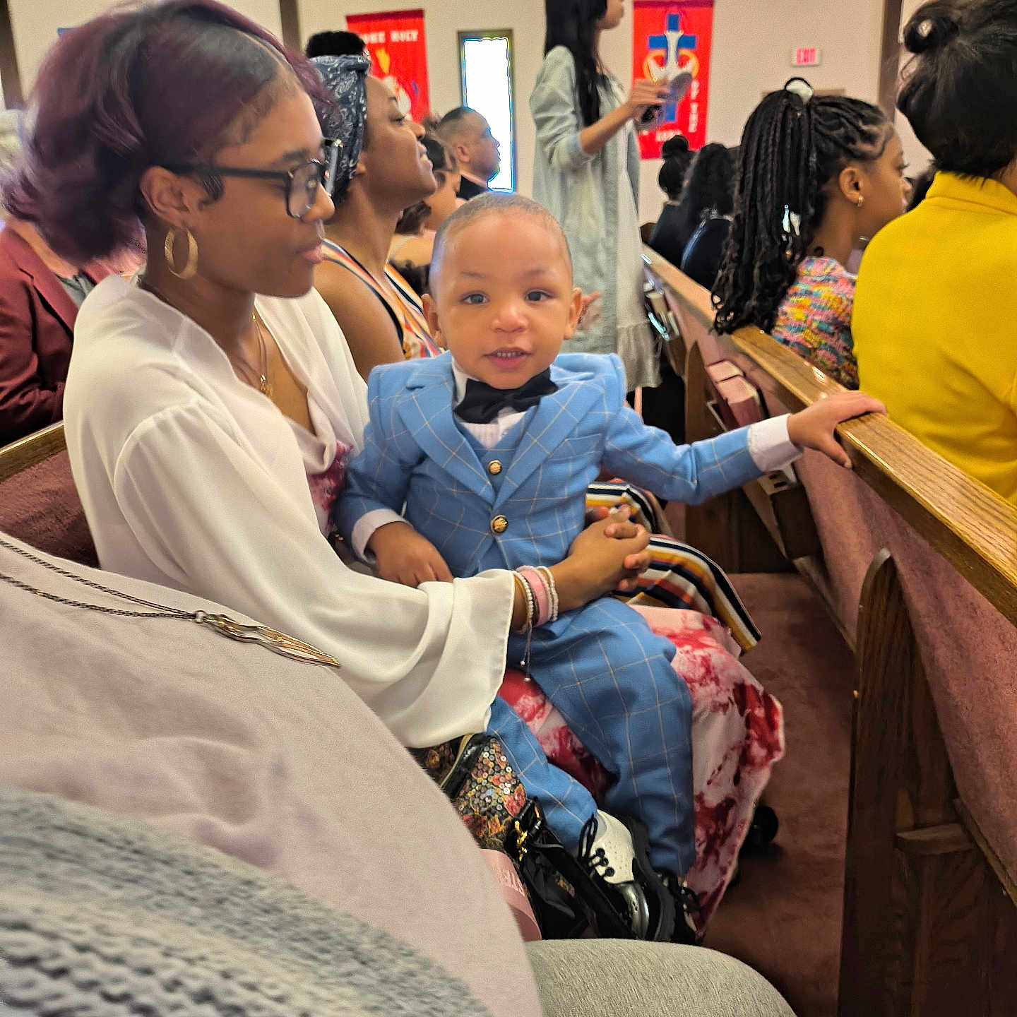 Kiondre joined the competition — help win amazing prizes! audience, bow_tie, child, church, event, formal_wear, glasses, hairstyle, holding, indoor, jewelry, multigenerational, people, pew, portrait, seated, smile, suit, toddler, woman