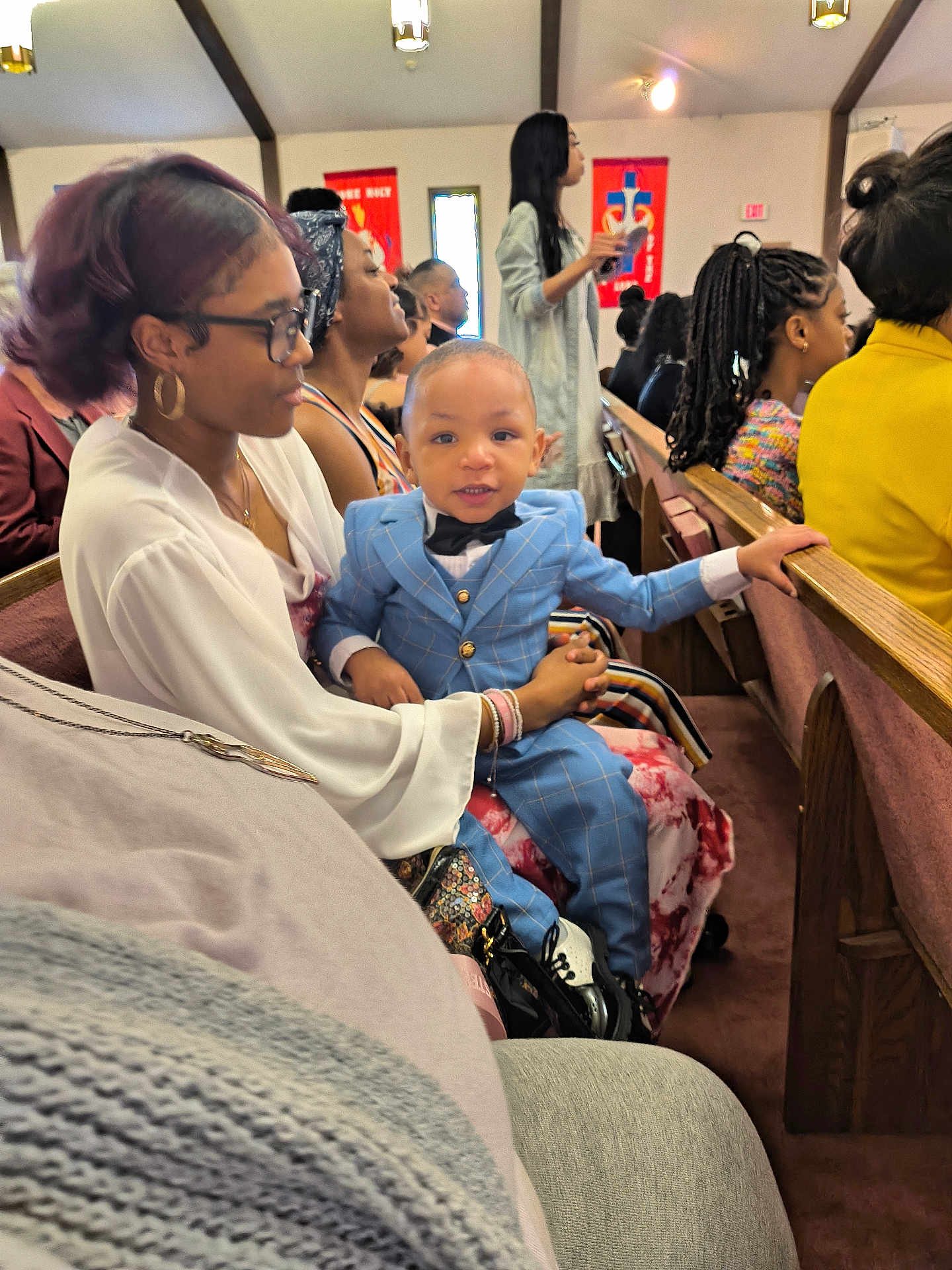 Kiondre joined the competition — help win amazing prizes! child, toddler, woman, glasses, suit, bow_tie, church, pew, people, indoor, seated, smile, formal_wear, audience, event, hairstyle, jewelry, holding, portrait, multigenerational
