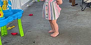 Hadleigh is registered to the contest to win money with this photo: barefoot, casual, child, concrete_floor, curious_expression, daylight, door, home, outdoor, person, plant, plastic_toy, playful, porch, railing, small_hair_ties, striped_dress, toddler, toys, wooden_chair