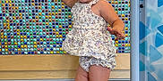 Hadleigh is registered to the contest to win money with this photo: background, child, colorful_wall, cute, floor, floral_outfit, hand_raised, happy, indoor, mosaic, person, play_area, shorts, sleeveless_top, smiling, standing, toddler, white_sandals, wood_floor, young_child