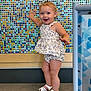 Hadleigh is registered to the contest to win money with this photo: background, child, colorful_wall, cute, floor, floral_outfit, hand_raised, happy, indoor, mosaic, person, play_area, shorts, sleeveless_top, smiling, standing, toddler, white_sandals, wood_floor, young_child