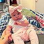 baby, infant, bow, headband, hand, tattoo, blanket, knitwear, pink, white, clothing, sitting, indoors, person, cute, soft_focus, toddler, bed, footwear, holding