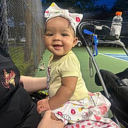 Nylani is registered to the contest to win money with this photo: adult, baby, bow, child, cute, drink_bottle, evening, hand, happy, headband, hello_kitty, outdoor, person, short_sleeve, skirt, smiling, sports, stroller, tattoo, tennis_court