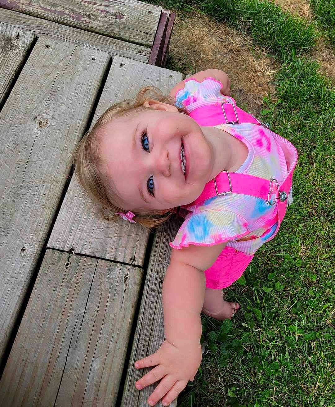 Maeva is registered to the contest to win money with this photo: baby_toddler_clothing, cheek, child, fun, grass, happy, hardwood, joy, leisure, lip, magenta, people_in_nature, person, pink, plank, plant, sitting, skin, smile, toddler