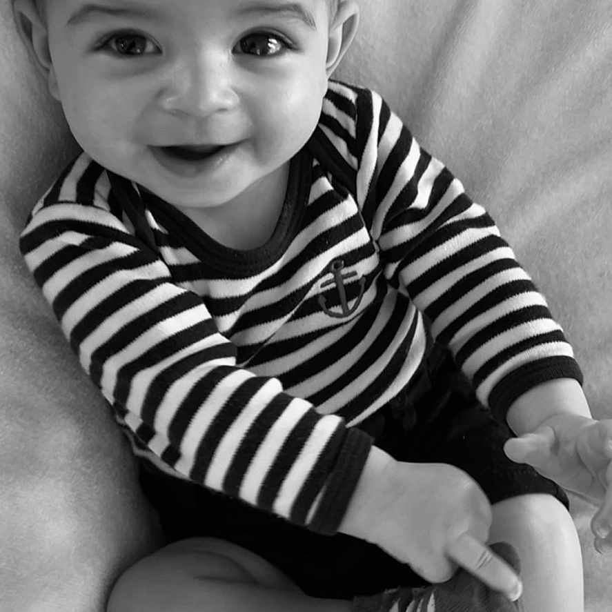 Gabriel a rejoint le concours — aidez-le/la à gagner de superbes lots ! baby, black_and_white, blanket, child, clothing, cute, face, footwear, happy, head, indoor, infant, person, playful, portrait, sitting, smiling, sock, striped_shirt, young