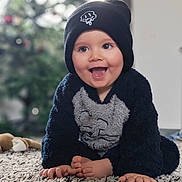 Elio participe au concours pour gagner de l'argent avec cette photo : child, baby, infant, smiling, tongue_out, beanie, hat, cozy_outfit, fuzzy_suit, carpet, rug, hands, toes, plush_toy, indoor, bokeh, christmas_tree, blurred_background, portrait, happy