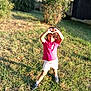 child, grass, outdoor, sunlight, greenery, shirt, shorts, sneakers, hands, heart_shape, standing, nature, daylight, happy, person, curly_hair, playing, summer, casual_clothing, park