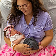 Vivian is registered to the contest to win money with this photo: woman, newborn, baby, pajamas, glasses, hospital, blanket, pink, bed, bedroom, bracelet, headband, sleeping, holding, person, indoor, curly_hair, family, mother, child