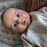 Mylann a rejoint le concours — aidez-le/la à gagner de superbes lots ! baby, blue_eyes, face, infant, blanket, cushion, soft_texture, clothing, cute, portrait, lying_down, child, indoors, cozy, skin, head, expression, newborn, warm, comfort