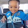 London is registered to the contest to win money with this photo: child, toddler, curly_hair, smiling, jacket, blue_jacket, car_interior, seat, seat_back, hand, playful, portrait, young_child, cute, person, happy, casual, daylight, window, car