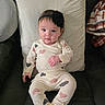 baby, infant, pajamas, heart_pattern, headband, flower, couch, pillow, blanket, indoor, child, person, seated, cute, looking_at_camera, home, cozy, soft_lighting, comfort, relaxed