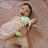 baby, child, smiling, happy, toy, stuffed_animal, pink_blanket, soft_texture, infant, cute, lying_down, playful, indoors, cozy, comfortable, pajamas, young_child, face, expression, joy