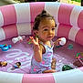 toddler, child, inflatable_pool, pink, white, water, toys, play, outdoor, curly_hair, topknot, summer, cute, sitting, colorful, plastic, fun, expression, small, pool