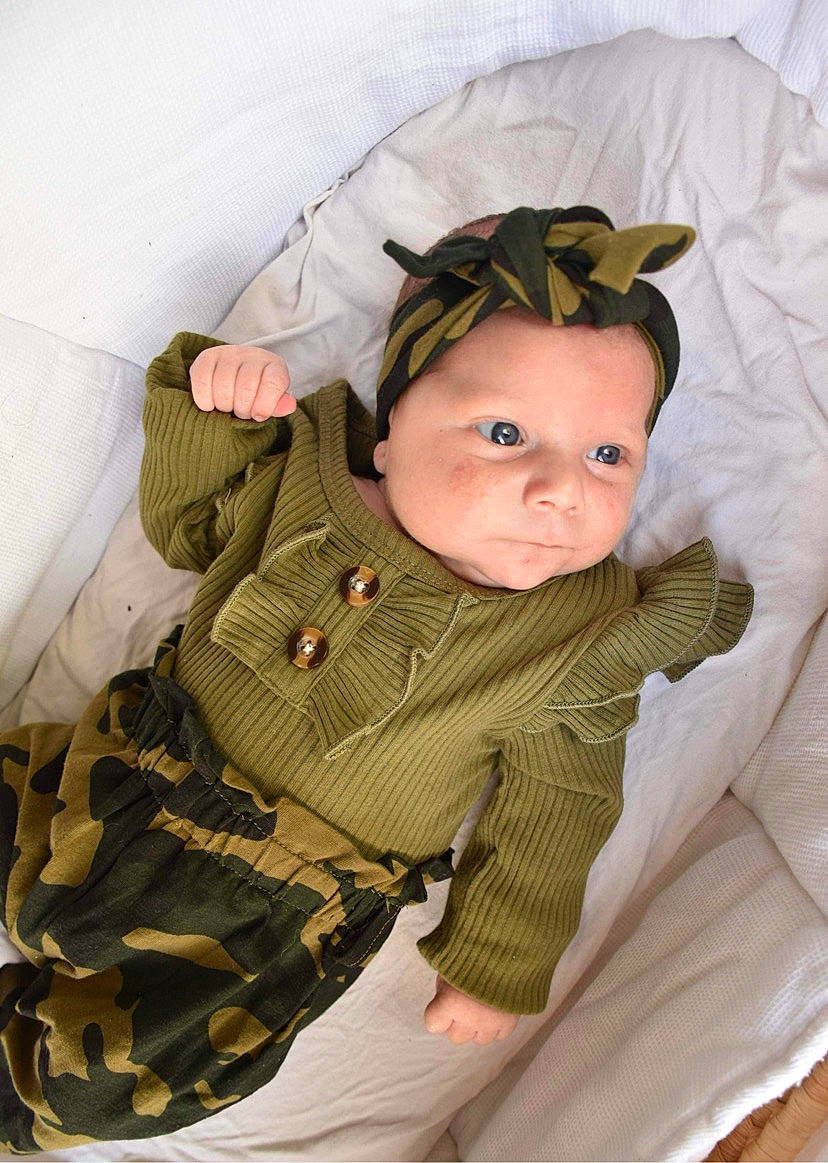 Kaëlya participe au concours pour gagner de l'argent avec cette photo : baby, baby_products, baby_toddler_clothing, camouflage, cheek, child, comfort, face, headgear, linens, military_camouflage, outerwear, pattern, person, sitting, skin, sleeve, textile, toddler, wood