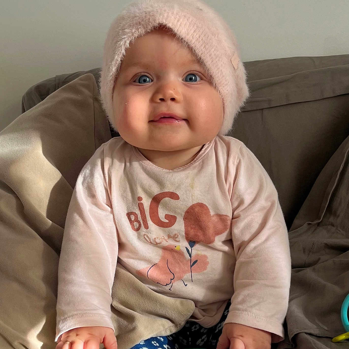 Edline a rejoint le concours — aidez-le/la à gagner de superbes lots ! baby, blue_eyes, child, clothing, cozy, cute, expression, face, furniture, hands, hat, indoor, infant, pillows, pink, shirt, sitting, sofa, toy, young_child