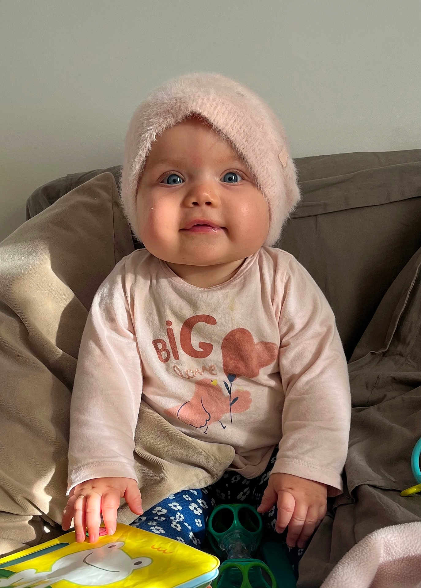 Edline a rejoint le concours — aidez-le/la à gagner de superbes lots ! baby, child, hat, pink, shirt, blue_eyes, sofa, pillows, toy, hands, sitting, indoor, cute, infant, face, clothing, cozy, expression, furniture, young_child