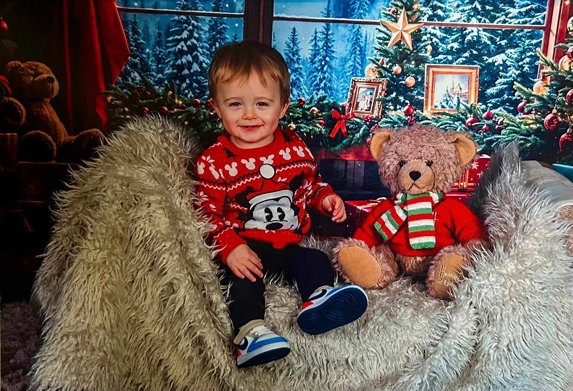 Luka is registered to the contest to win money with this photo: toddler, child, smiling, sweater, mickey_mouse, teddy_bear, christmas, holiday, decorations, chair, fluffy, shoes, indoors, portrait, festive, winter, pine_trees, scarf, red, cozy