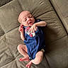 baby, newborn, infant, onesie, blue_clothing, couch, cushion, fabric, skin, foot, hand, face, person, lying_down, sleepy, indoors, soft_surface, cute, small, relaxed