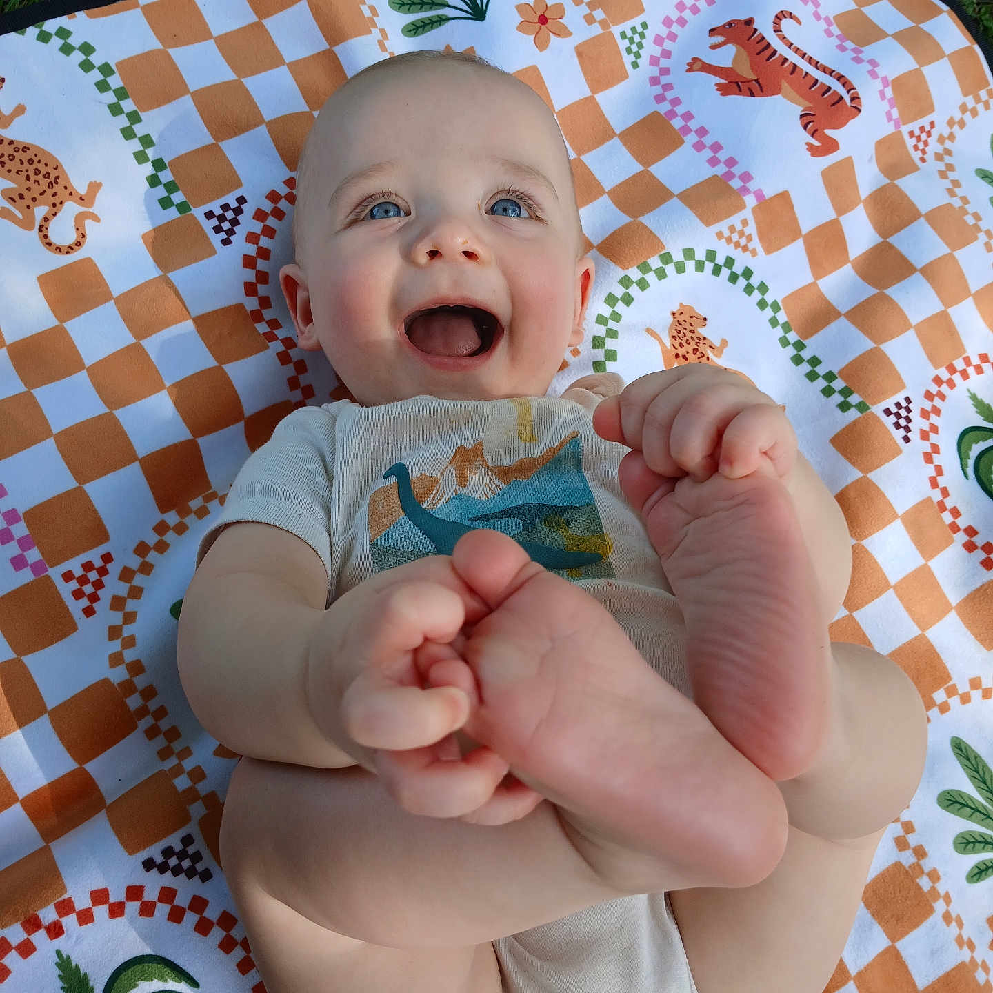 Ezra joined the competition — help win amazing prizes! baby, blanket, blue_eyes, child, clothing, cute, feet, grass, hand, happy, infant, lying_down, nature, outdoor, pattern, person, playful, skin, smiling, toddler