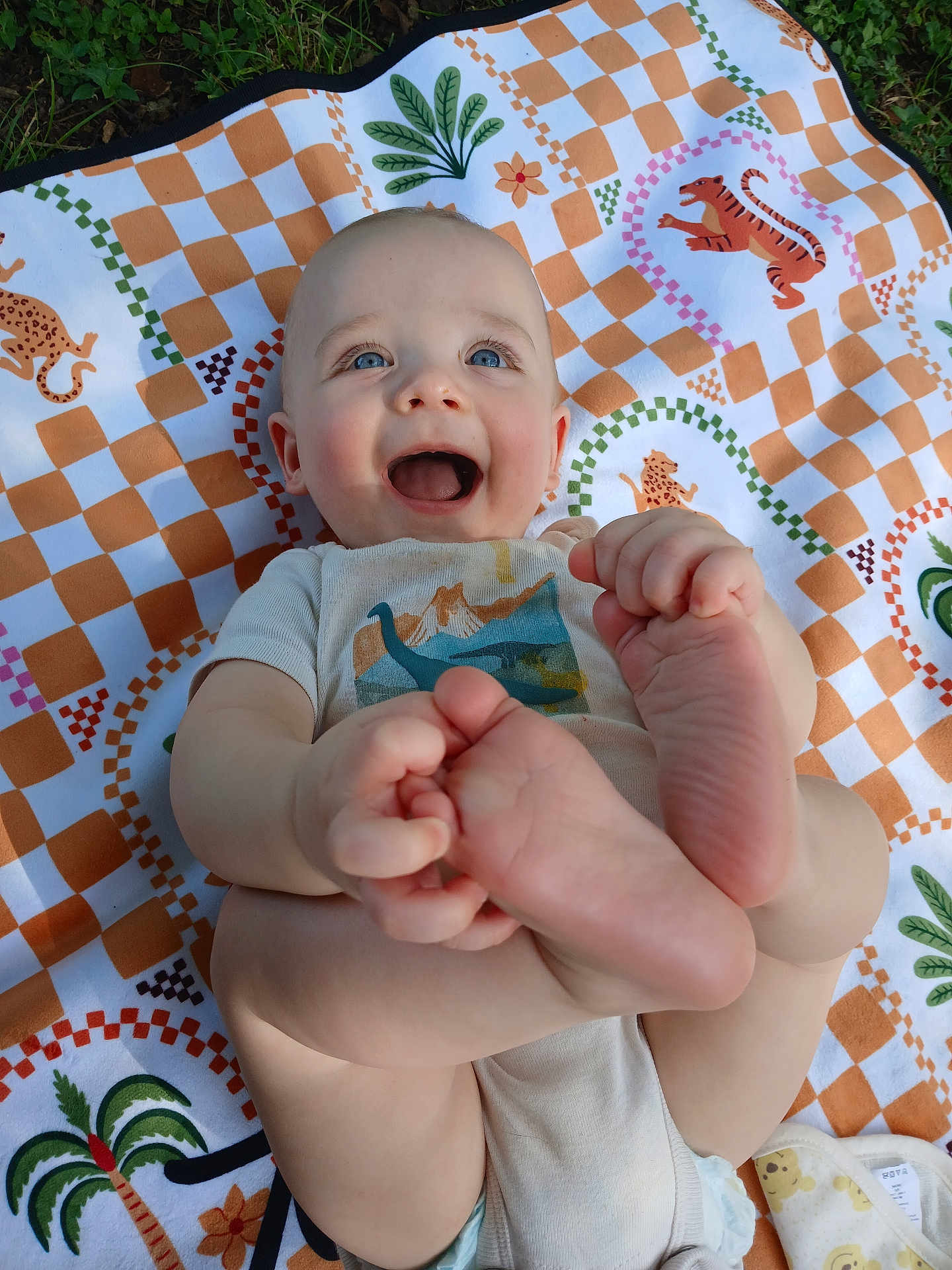 Ezra joined the competition — help win amazing prizes! baby, smiling, feet, hand, blanket, pattern, outdoor, grass, child, happy, cute, infant, playful, clothing, person, skin, blue_eyes, toddler, nature, lying_down