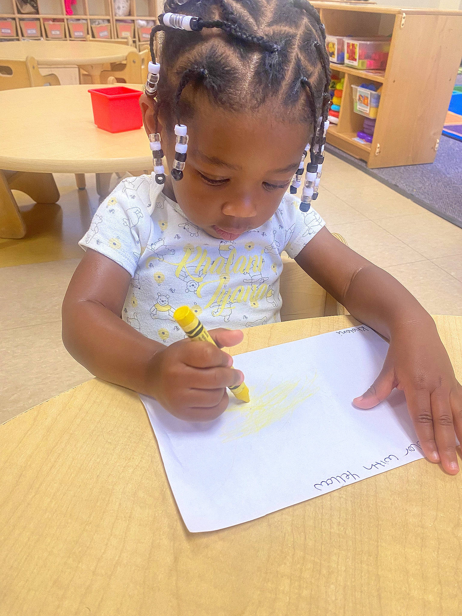 Khalani joined the competition — help win amazing prizes! baby, chair, child, desk, education, finger, flooring, fun, hair_tie, hand, office_supplies, person, play, room, shelf, sitting, table, toddler, wood, writing