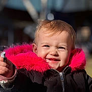 Lilou participe au concours pour gagner de l'argent avec cette photo : child, toddler, baby, smiling, toothy_grin, pink_fur, hooded_jacket, black_coat, close_up, portrait, outdoor, winter_clothing, hand, zipper, sunlight, rosy_cheeks, shallow_depth_of_field, happy, playground, blonde_hair