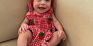 Blake joined the competition — help win amazing prizes! baby, smiling, red_bow, red_dress, strawberry_pattern, couch, beige, happy, child, infant, sitting, indoors, cute, portrait, headwear, feet, hands, skin, person, young_child