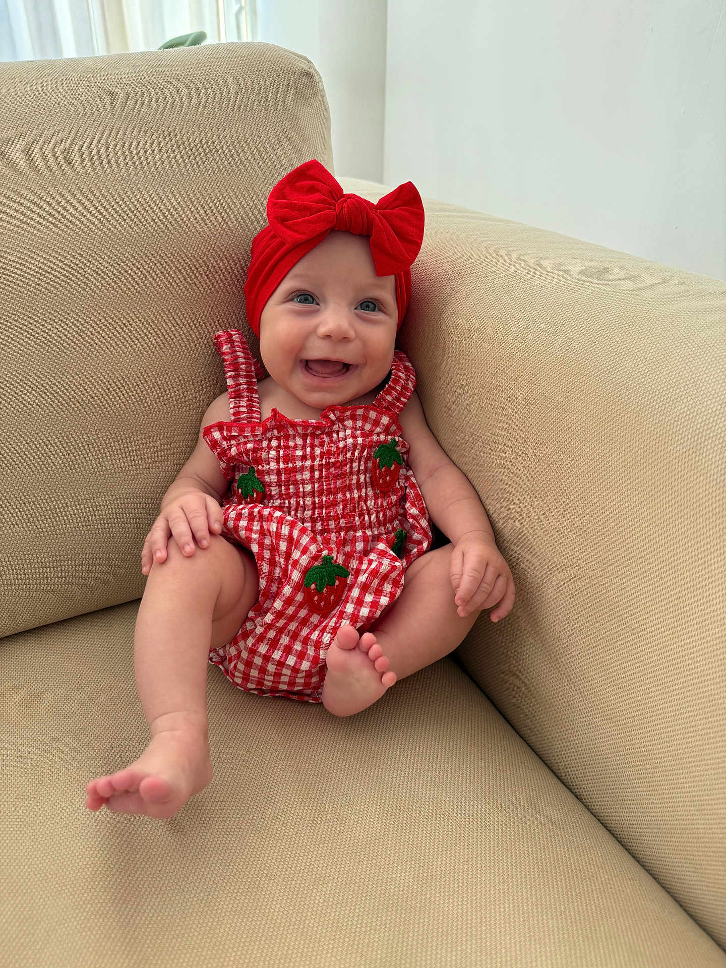 Blake joined the competition — help win amazing prizes! baby, smiling, red_bow, red_dress, strawberry_pattern, couch, beige, happy, child, infant, sitting, indoors, cute, portrait, headwear, feet, hands, skin, person, young_child