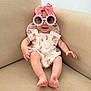 Blake is registered to the contest to win money with this photo: baby, child, sunglasses, headband, bow, romper, strawberry_pattern, couch, beige, smiling, indoor, cute, fashion, accessories, infant, sitting, feet, happy, portrait, playful