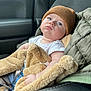 baby, child, car_seat, blanket, beanie, blue_eyes, white_shirt, quilted_jacket, cozy, indoor, car_interior, seatbelt, cute, portrait, warm_clothing, infant, comfort, soft_texture, casual, resting
