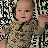 Waylon is registered to the contest to win money with this photo: baby, infant, onesie, vehicle_print, blanket, patterned_blanket, smiling, waving_hand, blue_eyes, cute, infant_clothing, lying_down, child, happy, indoors, soft_texture, closeup, face, human, young_child