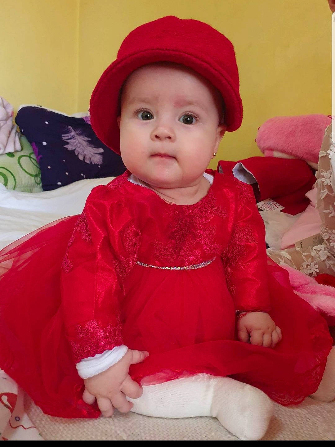 Anais participe au concours pour gagner de l'argent avec cette photo : baby, baby_toddler_clothing, cap, cheek, child, dress, embellishment, face, fashion_accessory, happy, headgear, headwear, linens, magenta, outerwear, pattern, person, pink, red, skin