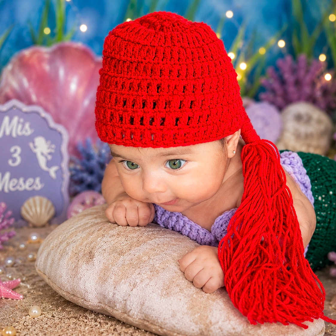 Hailey Trujillo is registered to the contest to win money with this photo: baby, child, red_hat, mermaid_costume, green_eyes, pillow, underwater_theme, decorations, purple_corals, starfish, seashells, pearls, lights, knitwear, cute, portrait, infant, costume, smiling, playful