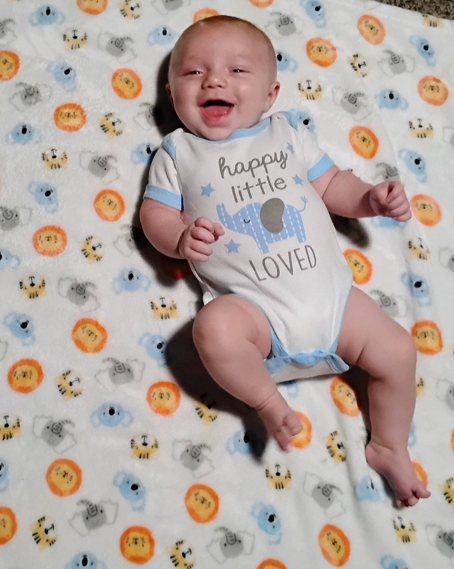 animal_pattern, baby, blanket, blue, child, cute, elephant, face, foot, gray, hand, happy, infant, lying_down, onesie, orange, patterned, skin, smiling, toddler