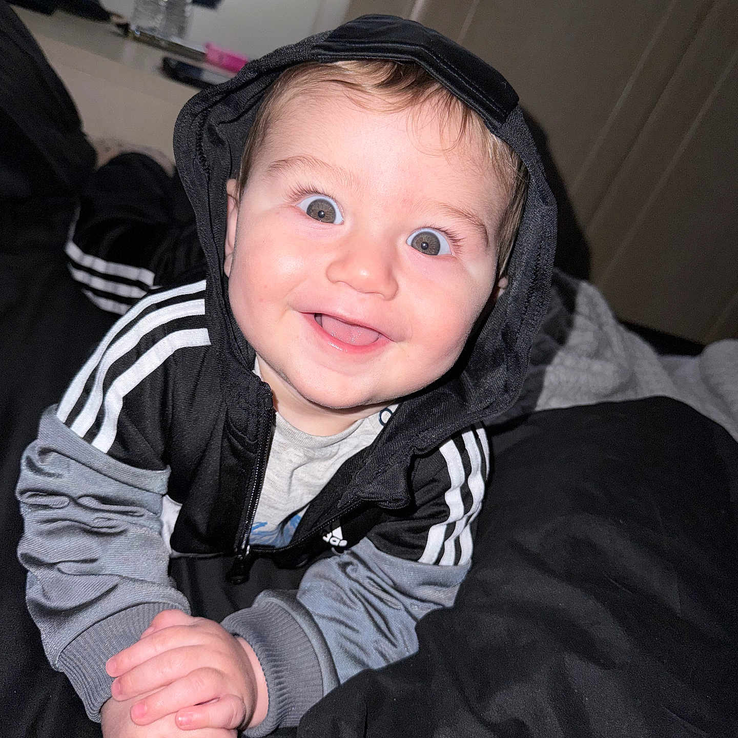 Marsh is registered to the contest to win money with this photo: baby, baby_face, bed, black_clothing, blanket, child, clothing, cute, eyes, face, gray_clothing, hands, happy, hoodie, indoor, infant, mouth, person, portrait, smiling