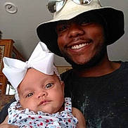Breanna is registered to the contest to win money with this photo: baby, bow, child, smile, man, hat, sunglasses, indoor, portrait, person, clothing, happy, face, holding, flower_pattern, headwear, family, casual, cute, infant
