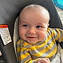 Finn is registered to the contest to win money with this photo: baby, child, smiling, striped_sweater, yellow, gray, face, closeup, infant, seated, happy, indoors, cushion, warning_label, clothing, person, portrait, cute, hand, young