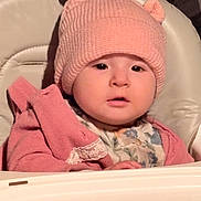 Clementine is registered to the contest to win money with this photo: baby, bear_ears, child, clothing, cozy, cute, expression, face, high_chair, indoor, infant, knit_hat, person, pink_hat, pink_jacket, portrait, seated, soft_lighting, warm_colors, young_child