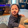 toddler, child, polka_dot, couch, living_room, rug, wooden_furniture, curtains, window, television, decor, portrait, indoor, smiling, hair, clothing, hand, face, person, cozy