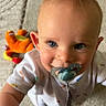 baby, blue_eyes, carpet, child, close_up, curious, cute, happy, indoor, infant, light, pacifier, person, plush_toy, smiling, soft_texture, toddler, toy, white_clothing, young_child