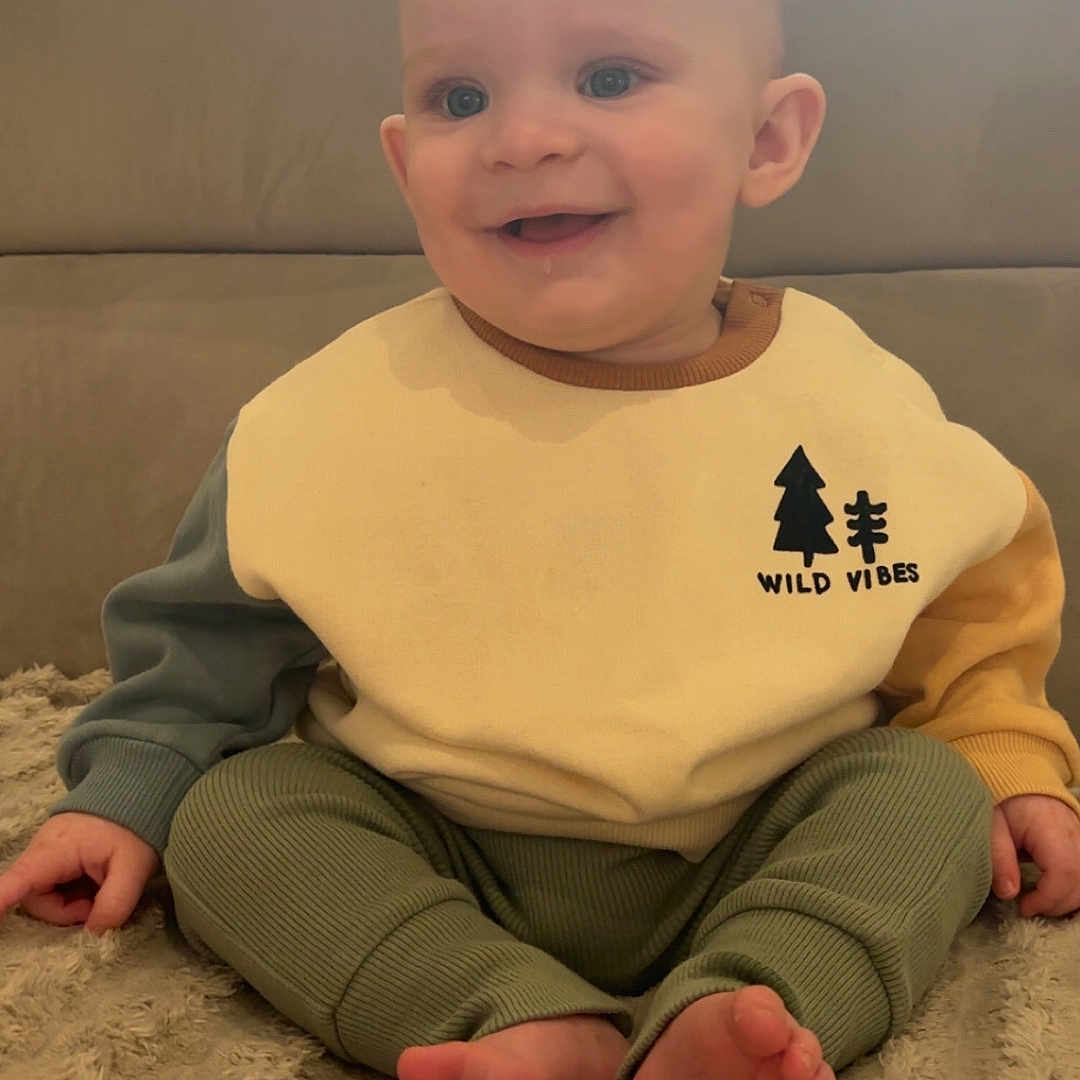 Tommy joined the competition — help win amazing prizes! baby, smiling, child, sitting, indoors, sweater, wild_vibes, feet, blanket, couch, window, happy, portrait, cozy, cute, clothing, infant, face, person, home