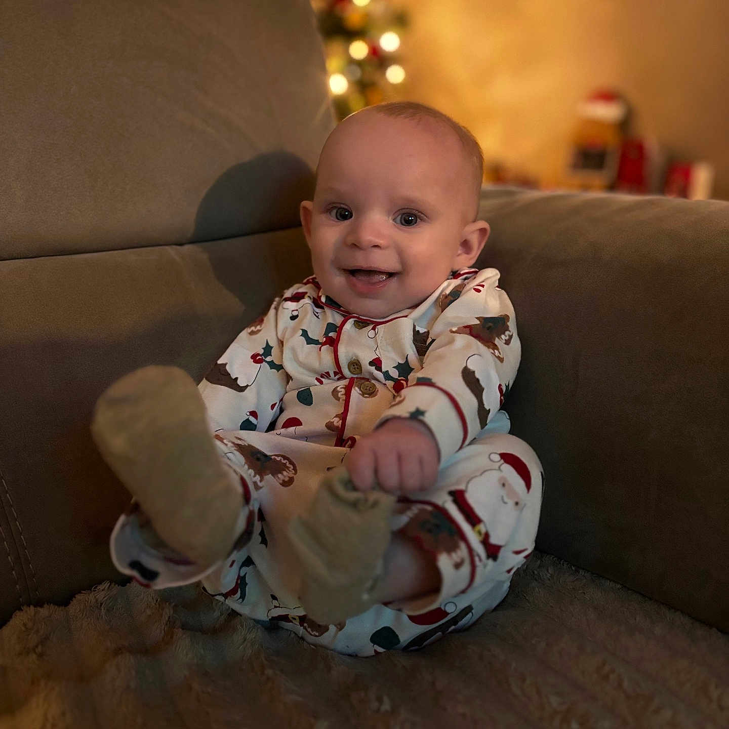 Tommy is registered to the contest to win money with this photo: baby, celebration, child, christmas_tree, couch, cozy, cute, decor, face, festive, happy, holiday, home, indoor, infant, pajamas, seated, smiling, soft_texture, warm_light