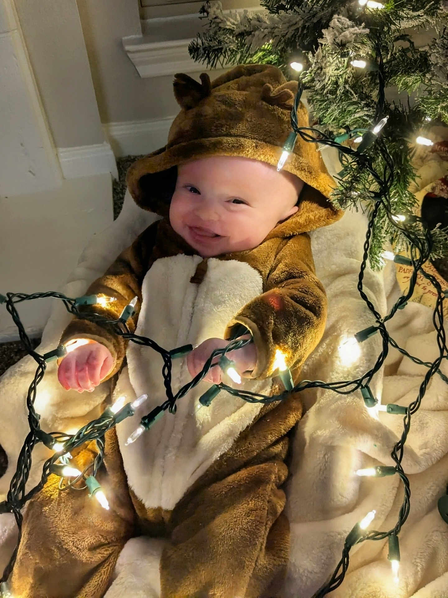 Owen is registered to the contest to win money with this photo: baby, child, infant, costume, reindeer, christmas_lights, holiday, festive, smiling, cute, blanket, indoors, decorations, tree, soft_texture, warm_clothing, happy, toddler, playful, celebration