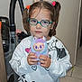 child, glasses, toy, plush_toy, indoor, vacuum_cleaner, mickey_mouse, minnie_mouse, pajamas, hair_ties, floor_tiles, door, sweatshirt, pants, person, face, hand, expressionless, standing, home