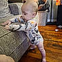 baby, baby_standing, basket, child, couch, dinosaur_pajamas, face, floor_lamp, foot, furniture, gray_couch, hand, home, indoor, interior, pajamas, person, standing, tissue_box, wooden_floor
