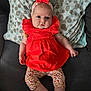 baby, infant, red_dress, headband, polka_dot_pillow, couch, indoor, legs, arms, face, serious_expression, clothing, patterned_leggings, child, person, sitting, cute, portrait, home, relaxing